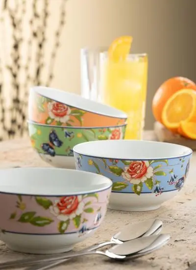 Three floral-patterned bowls on a kitchen counter, with a glass of lemonade, spoons, and fresh oranges in the background. the setting is softly lit, suggesting a warm, homey atmosphere.